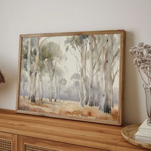 May include: A framed watercolour painting depicting a forest scene with tall, slender trees in shades of grey and brown. The trees are arranged in a loose, natural pattern, creating a sense of depth and perspective. The background is a soft, hazy blue, suggesting a distant horizon.