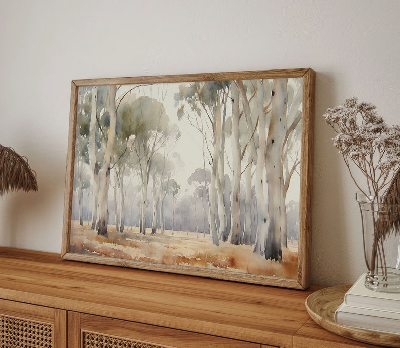 May include: A framed watercolour painting depicting a forest scene with tall, slender trees in shades of grey and brown. The trees are arranged in a loose, natural pattern, creating a sense of depth and perspective. The background is a soft, hazy blue, suggesting a distant horizon.