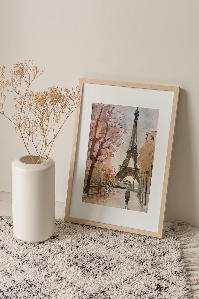 Puede incluir: Una pintura de acuarela enmarcada de la Torre Eiffel en Par&iacute;s, Francia. La pintura representa la torre con un cerezo en flor rosa y blanco en primer plano. Una sola persona camina en la distancia.