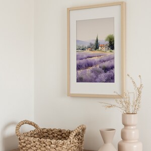 May include: A framed watercolor painting of a lavender field with a small house in the distance. The painting is hanging on a white wall above a wooden dresser with a woven basket and two ceramic vases.