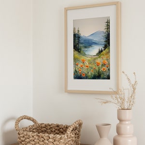 Puede incluir: Una pintura al agua enmarcada de una escena de lago de monta&ntilde;a con flores naranjas en primer plano. La pintura est&aacute; colgada en una pared blanca sobre una c&oacute;moda de madera con una cesta tejida y dos jarrones de cer&aacute;mica.