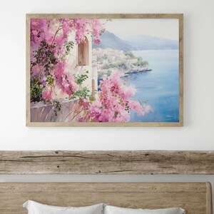 以下が含まれることがあります： ピンクの花が前景に咲き乱れ、青い海が背景に広がる、海岸の町の水彩画が額装されています。