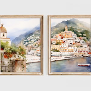 May include: Two watercolor paintings in wooden frames depicting a coastal town in Italy. The left painting shows a view from a balcony overlooking the town, while the right painting shows a wider view of the town and the sea.