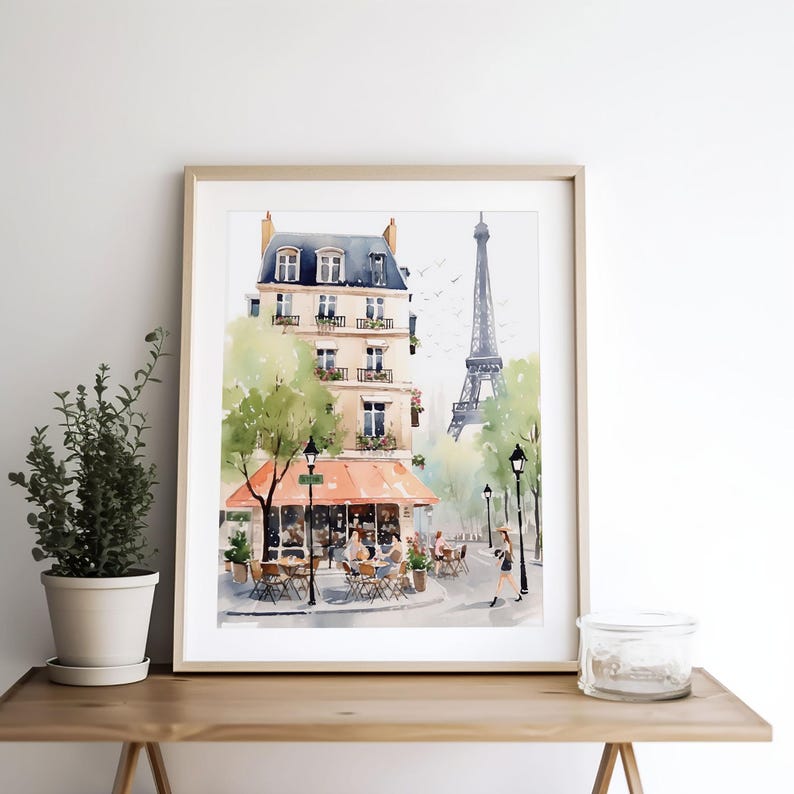 May include: Watercolor print of a Parisian street scene with a cafe, trees, and the Eiffel Tower in the background. The artwork is framed in a light wood frame and features soft colors.