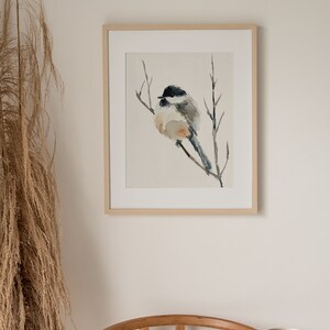Peut inclure: Une peinture &agrave; l'aquarelle encadr&eacute;e d'un petit oiseau perch&eacute; sur une branche. L'oiseau est gris et blanc avec une t&ecirc;te noire et une longue queue. L'arri&egrave;re-plan est beige clair.