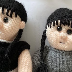 Peut inclure: Deux poupées en tricot avec des cheveux noirs en tresses, l'une portant une robe noire et blanche et l'autre un pull gris.