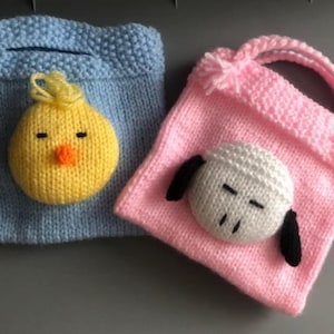 Op de afbeelding: Twee gebreide tassen met dierengezichten. De blauwe tas heeft een geel kuiken gezicht en de roze tas heeft een wit schapen gezicht.