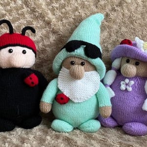 May include: Three knitted plush toys: a ladybug, a gnome wearing sunglasses, and a gnome with a flower on its hat. The ladybug is black with red spots and a red head. The gnome with sunglasses is wearing a green hat and a green outfit. The gnome with a flower is wearing a purple hat and a purple outfit.