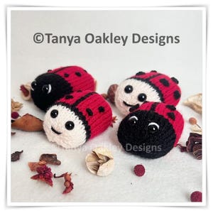 May include: Four handmade, knitted ladybugs with red and black bodies and white or black heads. Each ladybug has black spots and smiling eyes. The text "© Tanya Oakley Designs" is visible in the image.