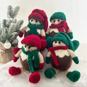 May include: Four knitted Christmas pudding ornaments with red and green hats, scarves, and mittens. The ornaments are sitting on a white surface.