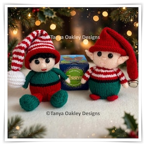 May include: Two handmade knitted elf dolls with black eyes and red mouths. One elf wears a red and white striped hat with a white pom-pom, the other a solid red hat with a silver bell. They sit beside a blue box labelled Terry's Chocolate Mint.