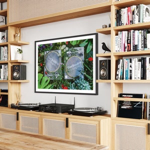 May include: Two black Technics turntables on a green and floral background. The turntables are on a shelf with a black framed picture above them. The shelf is part of a wooden bookcase with other bookshelves on either side.