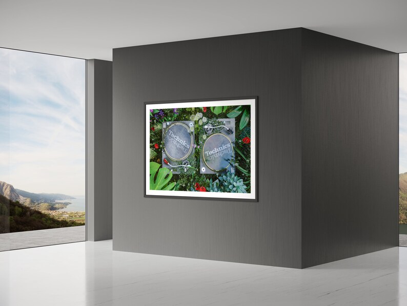 May include: Two black Technics SL-1200 turntables with silver platters are surrounded by green plants and flowers in a framed photograph.