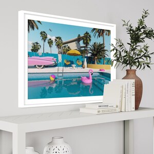 Pu&ograve; includere: Una stampa incorniciata di una casa moderna di met&agrave; secolo con una piscina, palme e un galleggiante a forma di fenicottero rosa. Una Cadillac rosa &egrave; parcheggiata accanto alla piscina.