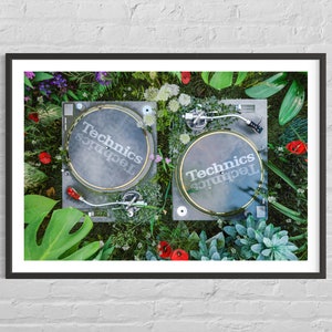 May include: Two black Technics turntables with gold accents are surrounded by green plants and flowers. The turntables are on a green surface.