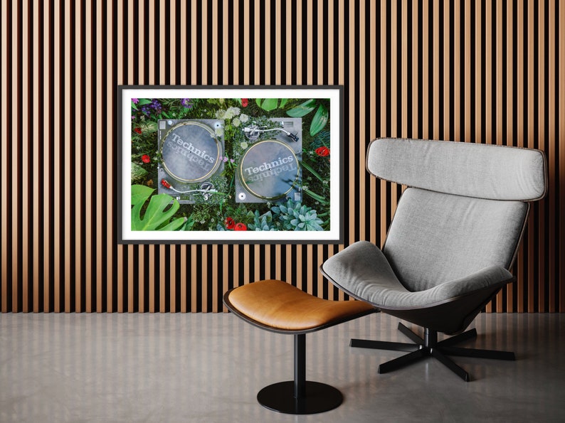 May include: Two black Technics turntables with white labels are surrounded by green leaves, red flowers, and succulents. The turntables are on a white surface. The image is framed in black.