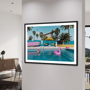 Pu&ograve; includere: Una stampa incorniciata di una casa moderna di met&agrave; secolo con una piscina. La piscina &egrave; circondata da palme e un'auto rosa. C'&egrave; un galleggiante rosa a forma di fenicottero nella piscina.