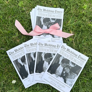 May include: A stack of wedding programs printed to look like a newspaper with the headline "The Wedding Times" and the text "TODAY IS THE BIG DAY!"  The programs feature a black and white photo of the couple and the text "ESTELLE & BENJAMIN The Wedding Times".