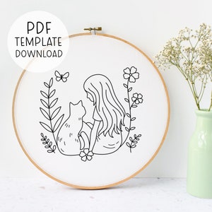May include: A black and white line drawing of a girl sitting with a cat in a field of flowers. The image is in a round embroidery hoop.
