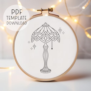May include: A black and white line drawing of a Tiffany style lamp with a decorative base and a shade with geometric patterns. The lamp is surrounded by small stars.