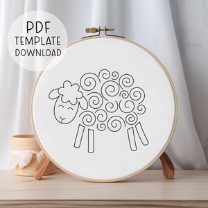 Pode incluir: Um desenho a preto e branco de uma ovelha com lã encaracolada, sobre um fundo branco num aro de bordado de madeira.