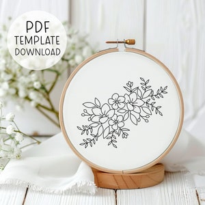 May include: A black and white line drawing of a floral bouquet on a white embroidery hoop. The hoop is made of wood and has a natural finish.