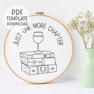 May include: A white embroidery hoop with a black line drawing of a glass of wine on top of a stack of books. The text "Just One More Chapter" is written around the wine glass and books.