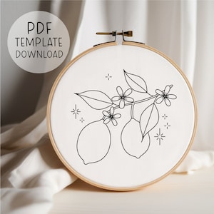 May include: Black and white line art embroidery pattern of a lemon branch with leaves and flowers. The pattern is displayed in a wooden embroidery hoop.