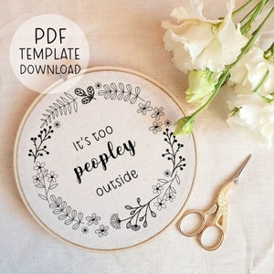 May include: A white embroidery hoop with a black floral design and the text "It's too peopley outside".
