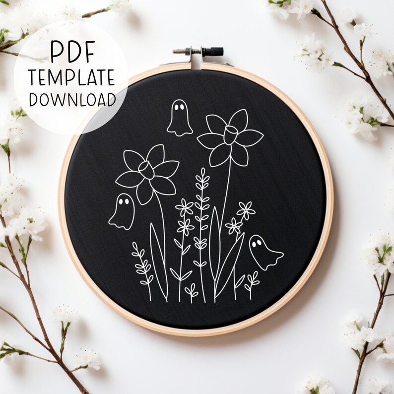May include: Black embroidery hoop with white outline of a floral design with ghosts. The design includes daffodils, small flowers, and leaves.