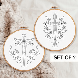 May include: Set of two embroidery hoop art prints. One features a dragonfly with a sword, the other a sword with floral accents. Both are in black and white.