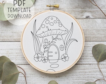 May include: A black and white line drawing of a mushroom house with a door, windows, and a vine. The mushroom house is surrounded by flowers and grass. The drawing is on a white fabric in a wooden embroidery hoop.