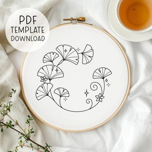 May include: A black and white embroidery pattern of ginkgo leaves and flowers on a white fabric stretched in a wooden embroidery hoop.