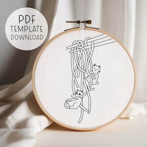 Puede incluir: Dibujo en blanco y negro de dos gatos colgando de un manojo de fideos sostenidos por palillos. La imagen est&aacute; en un lienzo blanco en un aro de bordado de madera.