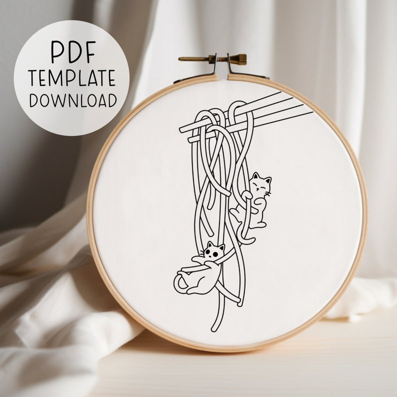 Puede incluir: Dibujo en blanco y negro de dos gatos colgando de un manojo de fideos sostenidos por palillos. La imagen est&aacute; en un lienzo blanco en un aro de bordado de madera.