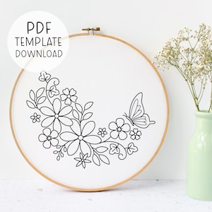May include: A black and white embroidery pattern of a butterfly and flowers on a white fabric in a wooden embroidery hoop.