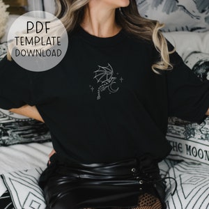 Op de afbeelding: Een zwart T-shirt met een witte omtrek van een draak die over een halve maan met sterren vliegt. De tekst "PDF TEMPLATE DOWNLOAD" staat in een witte cirkel in de linkerbovenhoek van de afbeelding.
