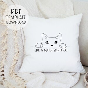 Puede incluir: Almohada blanca con un dibujo de l&iacute;nea negra de un gato mirando por encima de una superficie con el texto "La vida es mejor con un gato".