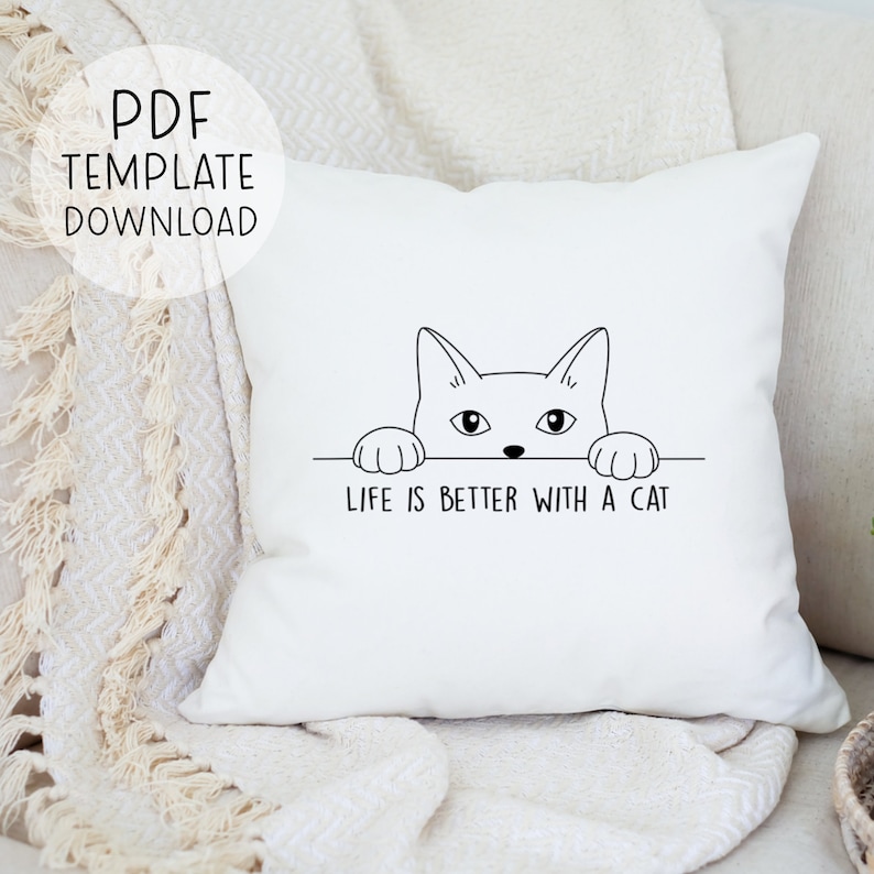 Puede incluir: Almohada blanca con un dibujo de l&iacute;nea negra de un gato mirando por encima de una superficie con el texto "La vida es mejor con un gato".