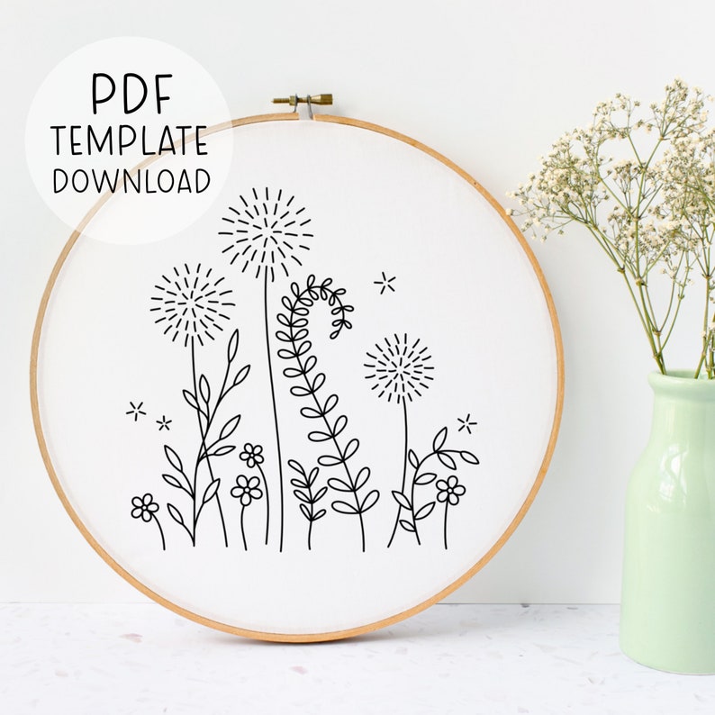 May include: A black and white embroidery pattern of a floral design with dandelions and leaves. The pattern is displayed in a wooden embroidery hoop.