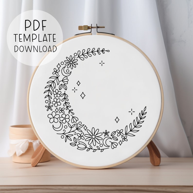 May include: A black and white embroidery pattern of a crescent moon with floral details, stars, and leaves. The pattern is displayed on a white embroidery hoop.