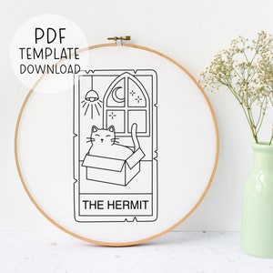 May include: An embroidery hoop with a white fabric featuring a black line drawing of a cat in a box, a window with a moon and stars, and the text "THE HERMIT". The text "PDF TEMPLATE DOWNLOAD" is above the design.