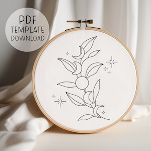 Puede incluir: Un dibujo en blanco y negro de un diseño de luna y hojas en un aro de bordado. El diseño presenta una rama con hojas y lunas crecientes, junto con una estrella.