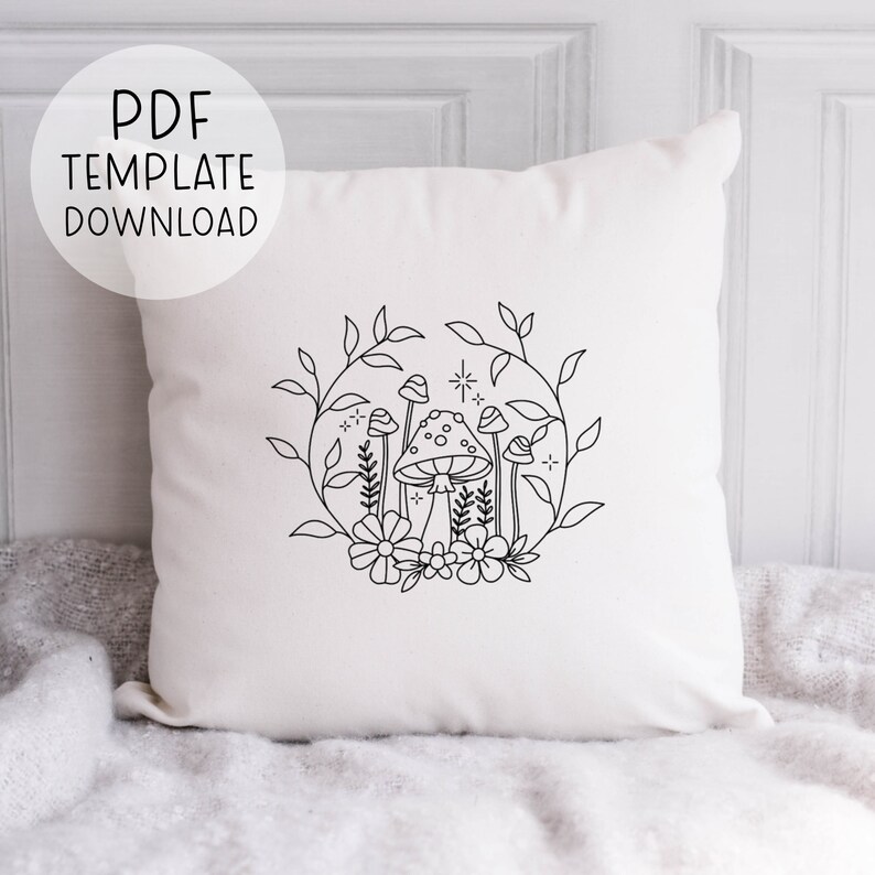 May include: A white cushion featuring a black line drawing of mushrooms and flowers within a circle. The design is simple and minimalist.