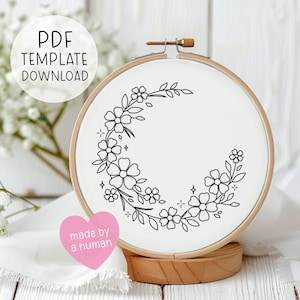 Könnte beinhalten: Ein weißer Stickrahmen mit einem Blumendesign in schwarzer Tinte. Der Text "PDF TEMPLATE DOWNLOAD" befindet sich in einem weißen Kreis. Ein rosa Herzaufkleber lautet "made by a human". Der Rahmen steht auf einem Holzsockel.