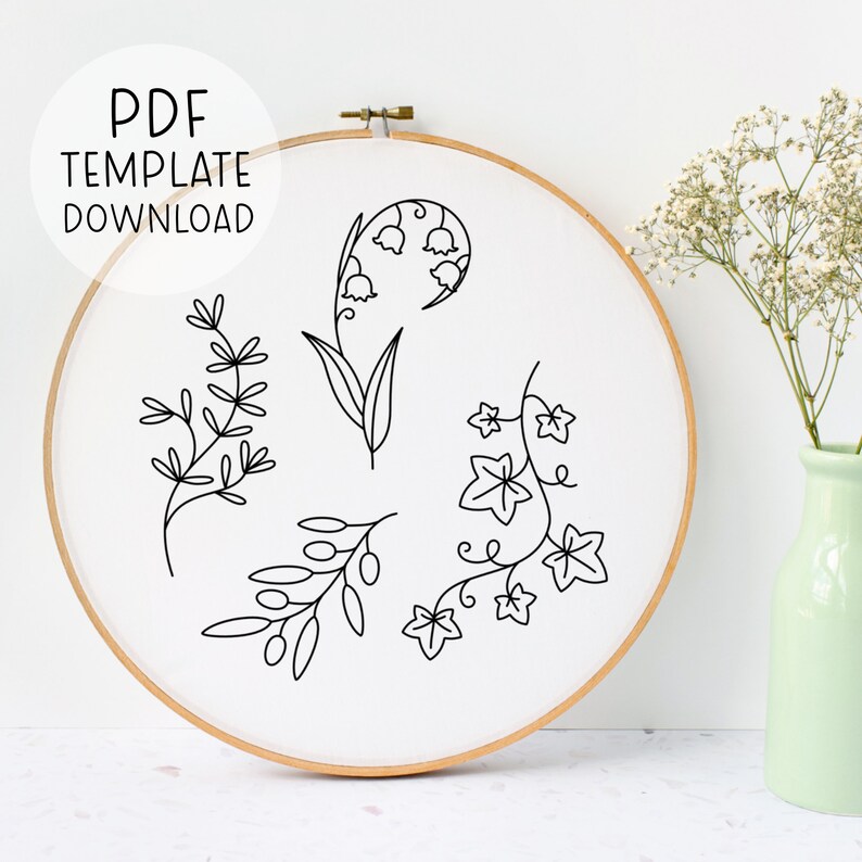 Pode incluir: Um padr&atilde;o de bordado preto e branco com quatro desenhos florais diferentes: l&iacute;rios do vale, hera, ramos de oliveira e um galho simples. O padr&atilde;o &eacute; exibido em um tecido branco esticado sobre um aro de bordado de madeira.