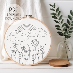 以下が含まれることがあります： 虹、雲、花が描かれた白黒の刺繍枠のデザイン。初心者向けの刺繍プロジェクトに最適です。