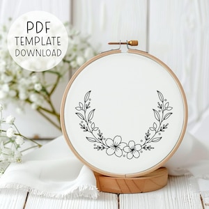 Könnte beinhalten: Ein schwarzer und weißer Stickrahmen mit einem floralen Design. Das Design zeigt zwei Blumen und Blätter.