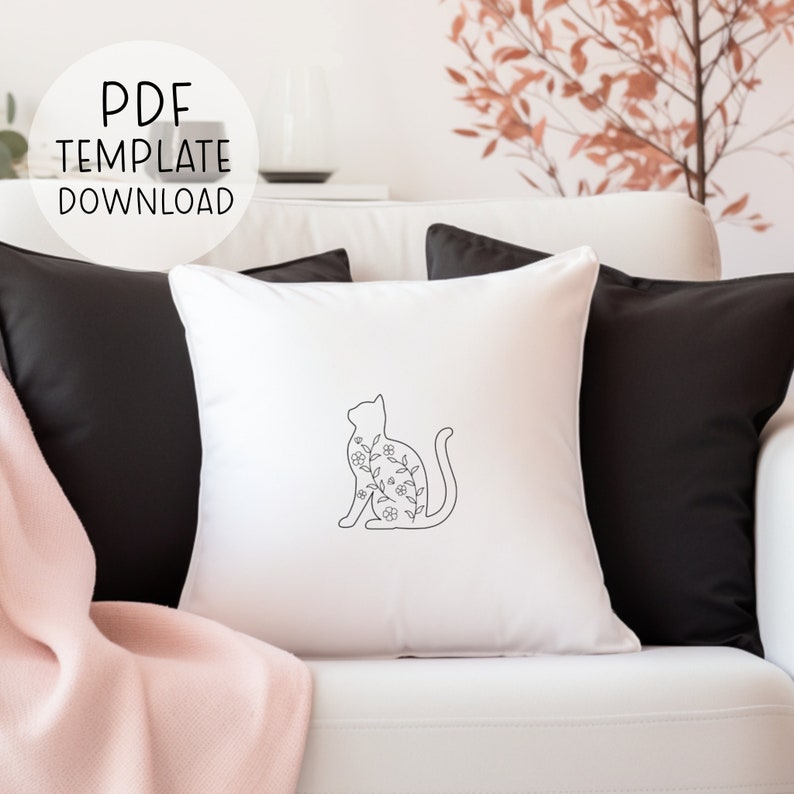 May include: White throw pillow with a black outline of a cat with floral details inside the outline. The pillow is on a white couch with black throw pillows.