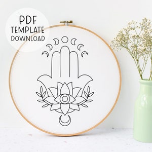 May include: A black and white line drawing of the Hamsa hand with a stylized eye in the center of a lotus flower. The Hamsa hand is surrounded by crescent moons.